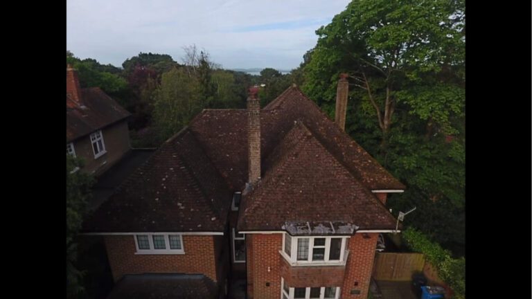 Red brick home with dark tiled roof covered in moss from the front